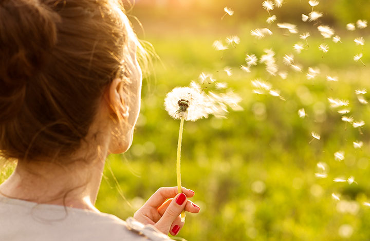 Frau pustet an einer Blume.